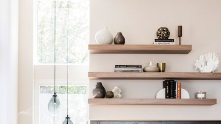 Floating wooden shelves minimally styled in modern living room with fabric chair, glass side table and black painted fireplace