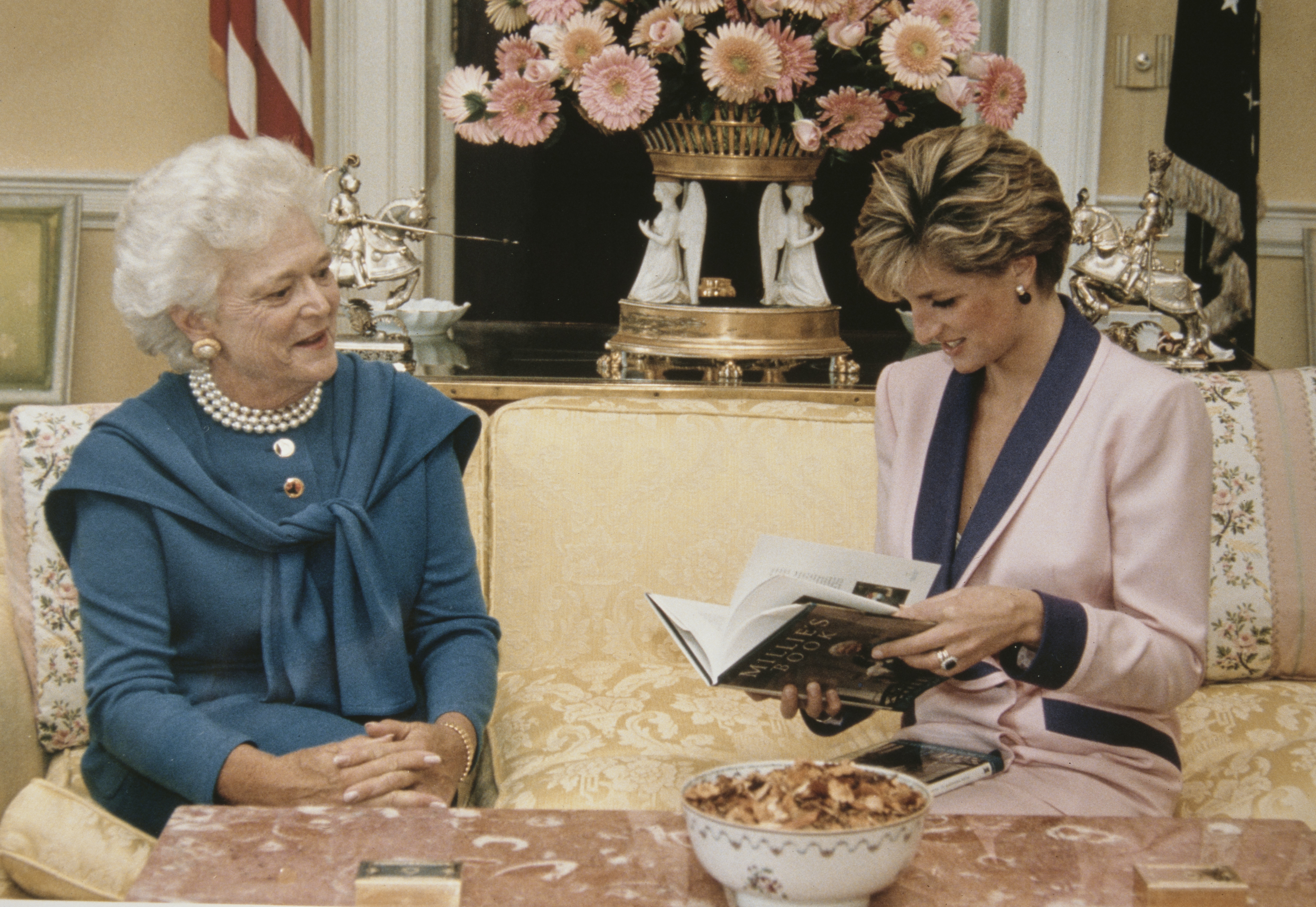 Barbara Bush sitting on a sofa with Princess Diana looking at a book