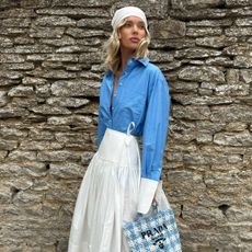 Elsa Hosk wearing a head scarf, Helsa blue button-down shirt and white poplin midi skirt, and Alaia fishnet slippers in the Cotswolds