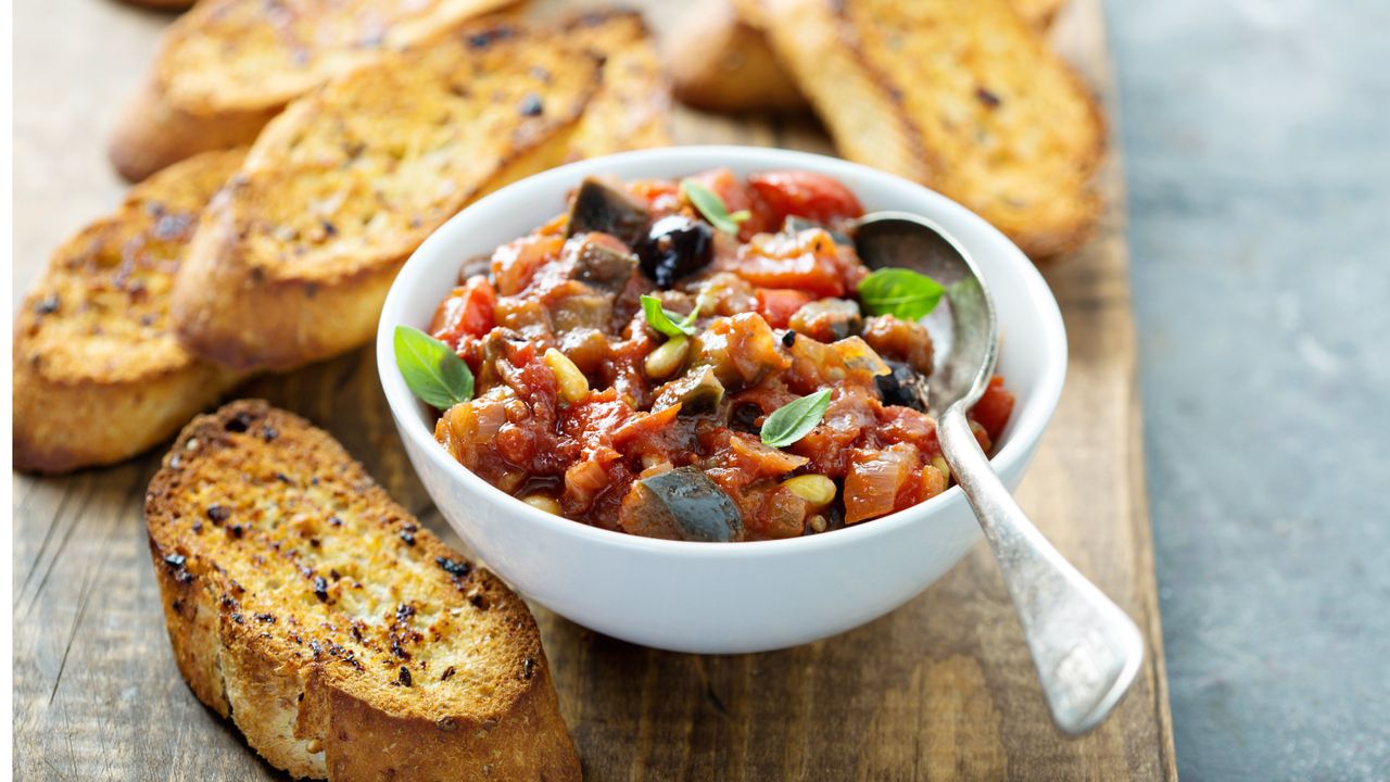 Bowl of aubergine caponata pasta with slices of baguette