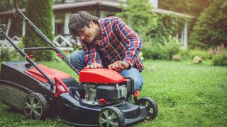 Man bending down on grass looking at red lawn mower.