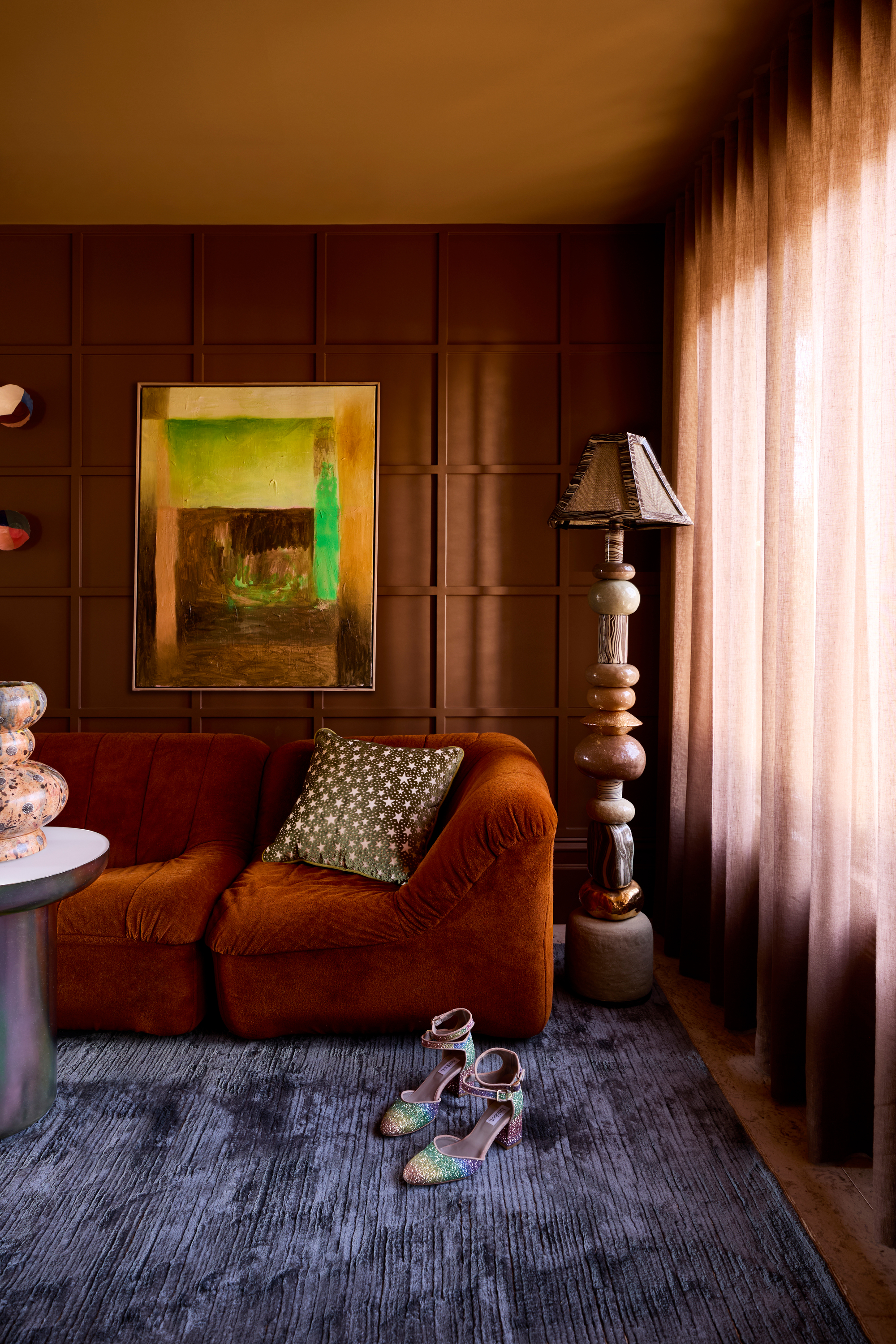 a color drenched living area with a rust velvet sofa, timber wall detailing and dark blue rug