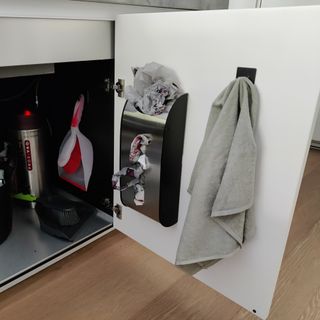 Under sink cupboard with hooks on door storing towel and carrier bags