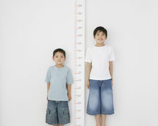 two brothers comparing their height against a height measure