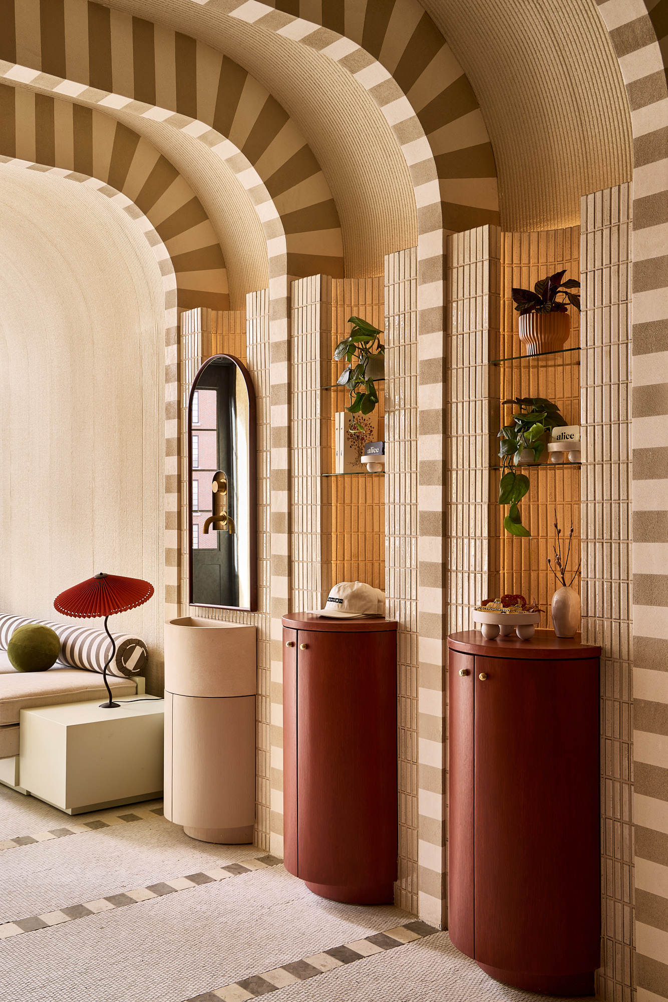 A pastel-hued hotel lobby with curated shelves and tiled, arched walls.