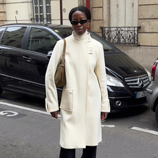 Girl with white maxi coat and sunglasses standing on Parisian seat.