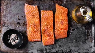Three salmon pieces on cast iron tray with olive oil, salt and pepper