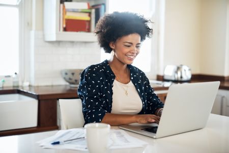 A smiling woman working on her laptop in her living room, filing her taxes