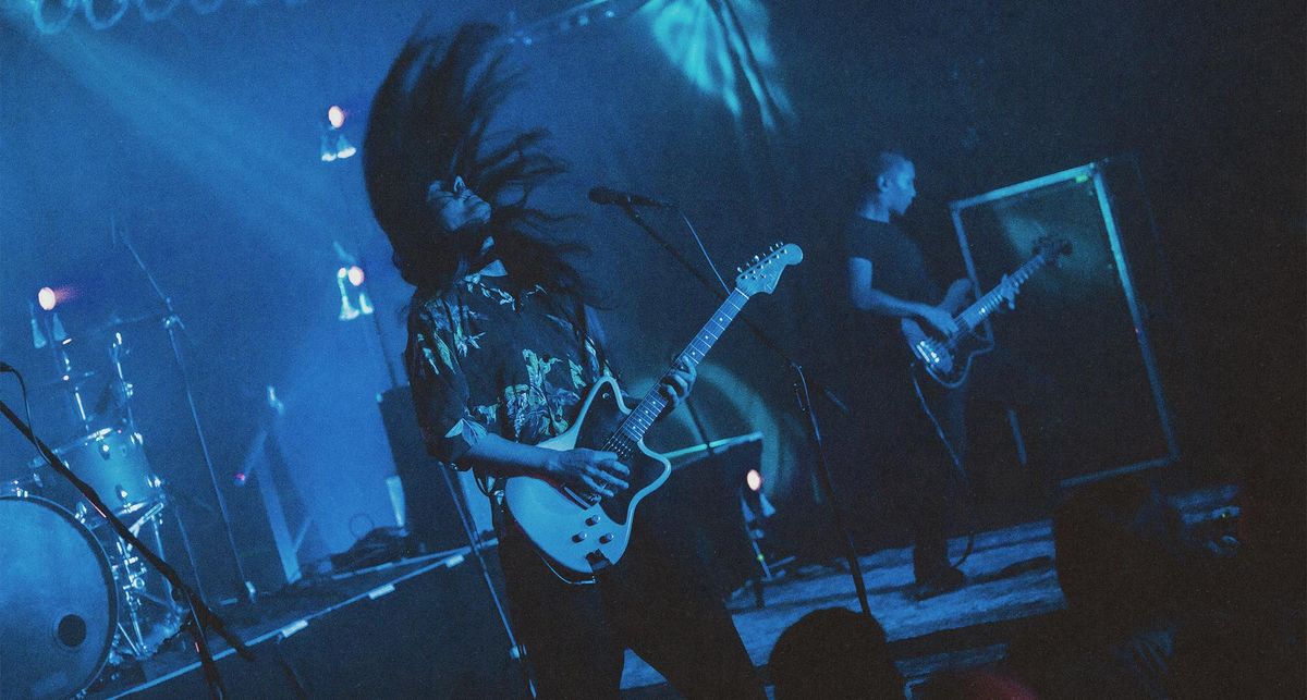 Neige of Alcest headbangs whille playing a Fender Toronado onstage, in an image that is rendered in blue and black from the stagelights.