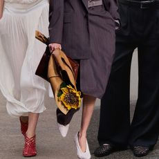 The woven shoe trend is shown in a collage of close runway and street-style images with a model on the left wearing a white dress with red woven shoes, a model in the middle wearing a gray skirt suit with white woven heels and a woman on the right wearing black trousers with black woven flats 