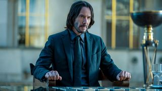 John (Keanu Reeves) sits at a table in John Wick: Chapter 4.