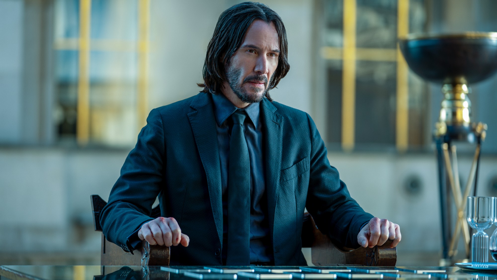John (Keanu Reeves) sits at a table in John Wick: Chapter 4.