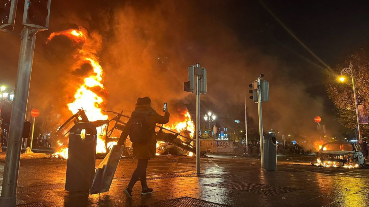 A woman crosses the road at night as a fire blazes in the middle of Dublin 