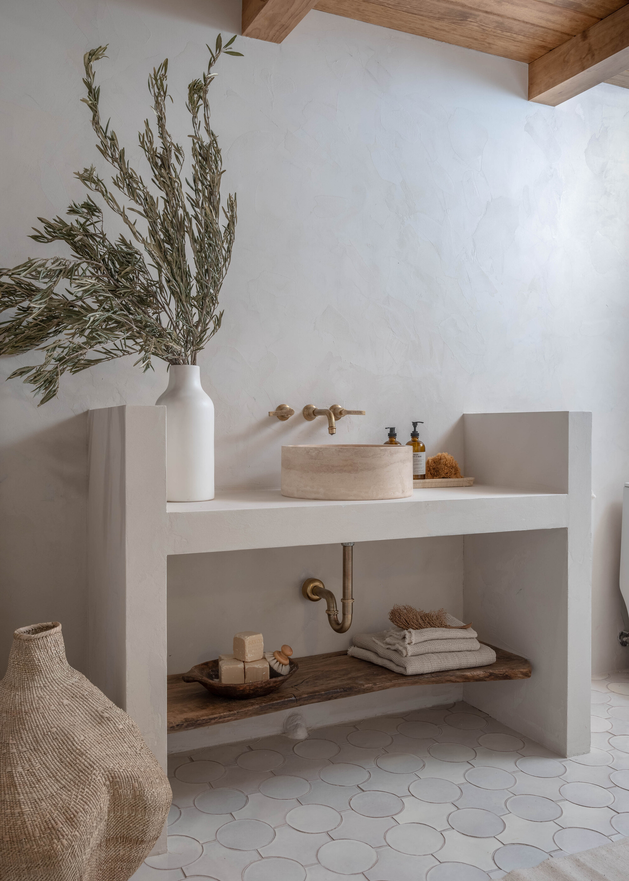 A bathroom with grey tiled flooring, a minimalist vanity, and a stone sink