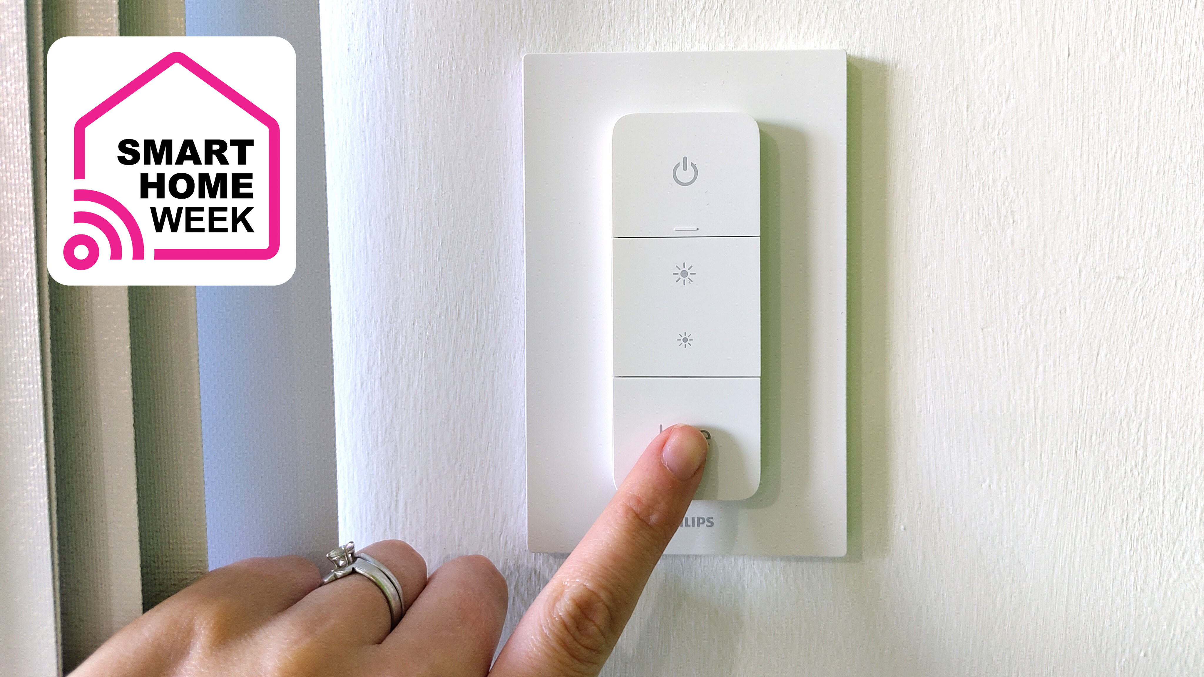 Woman&#039;s hand pressing Philips Hue Dimmer Switch on wall
