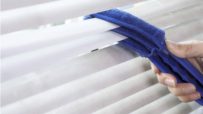 A three-tiered duster being used to clean blinds.