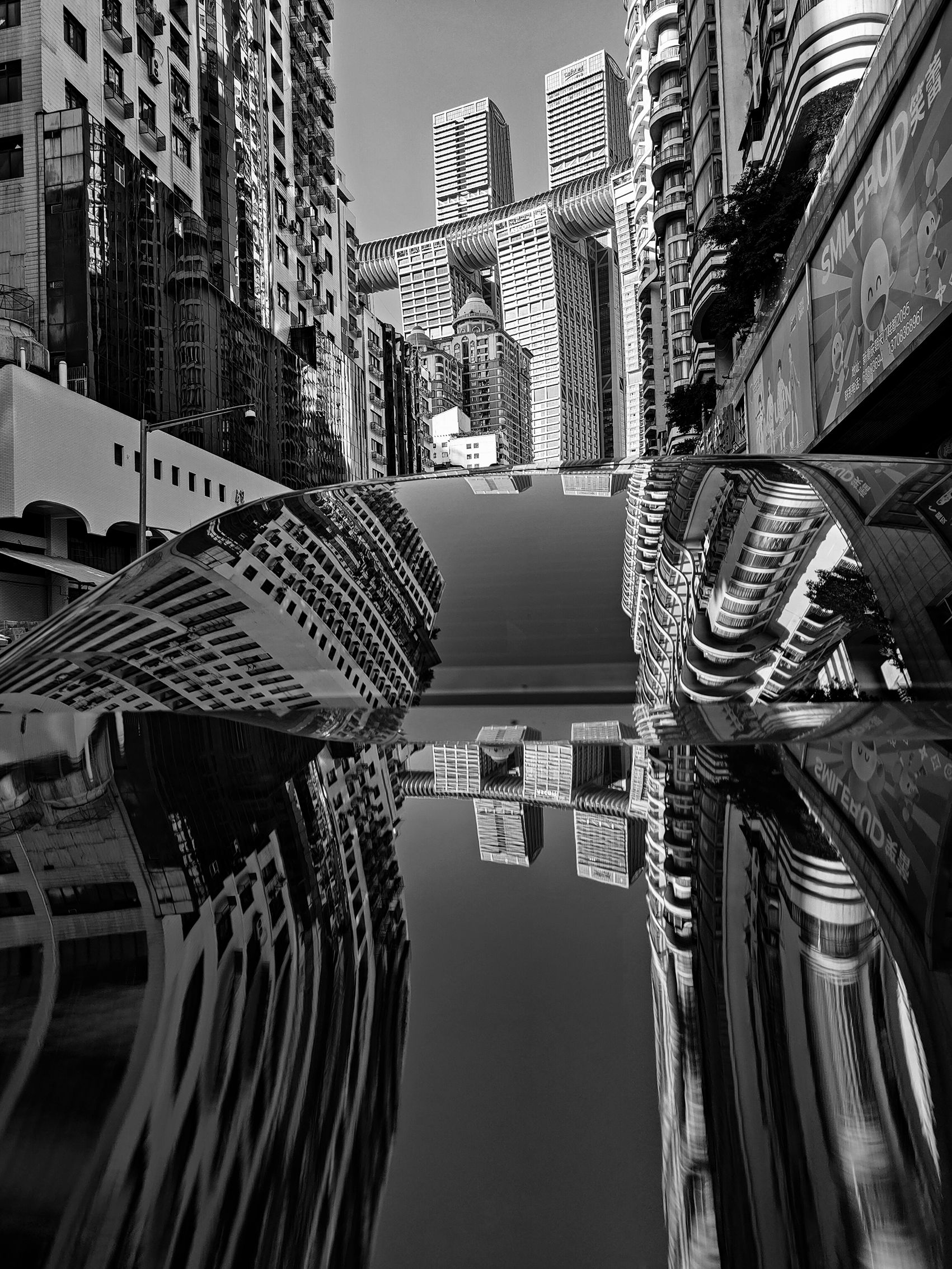Black and white photo of skyscrapers reflected in a car roof, creating a surreal, mirrored effect, tall buildings line the street