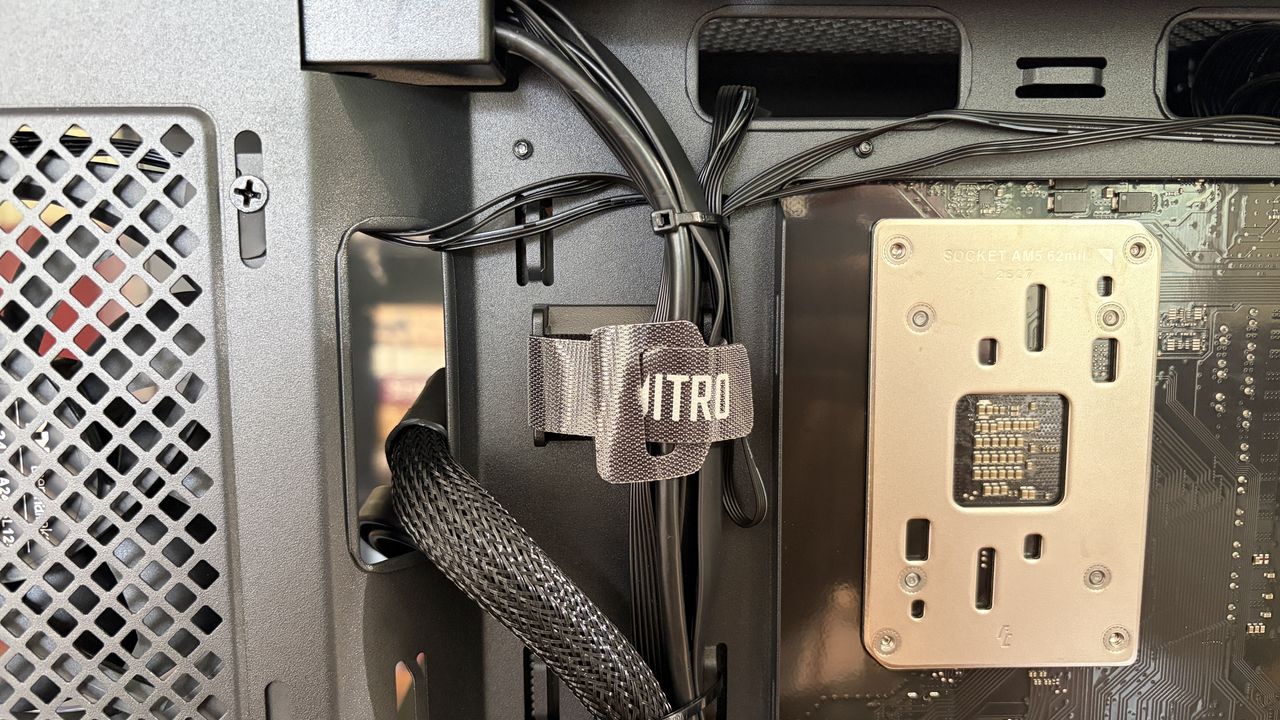 Interior view of a Nitro 65 computer case showing cables, an "ITRO" strap for cable management, and a metal CPU socket bracket labeled "SOCKET AM5 62mm."