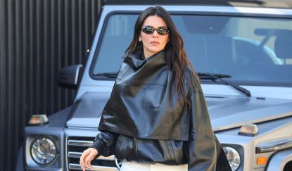 Kendall Jenner in a black leather bomber jacket, white pants, and bag, by Phoebe Philo