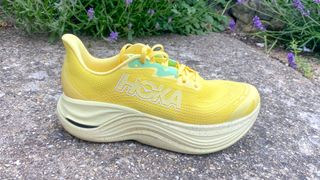 The Hoka Skyward X in front of some flowers on a sidewalk