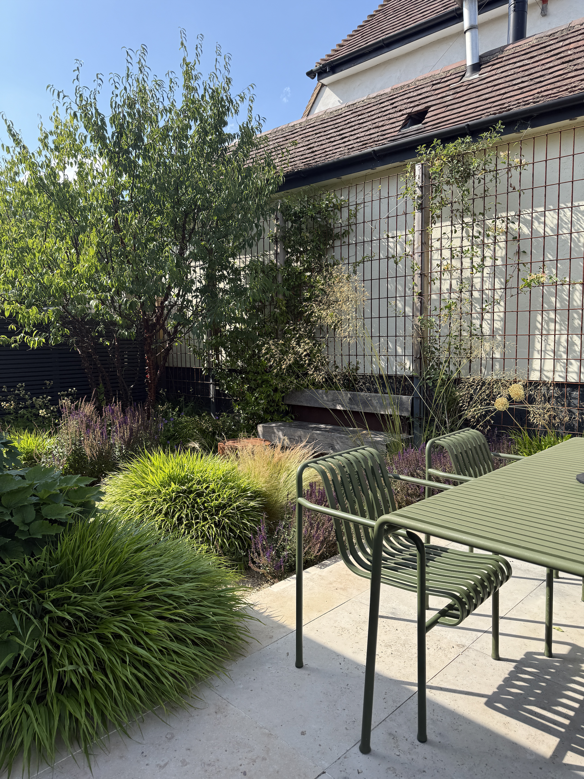Immersive courtyard garden with Hay Palissade furniture in green, lush grasses, gravel paths and steel mesh trellis