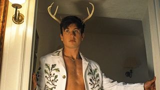 A still from the movie Saltburn of actor Barry Keoghan as Oliver Quick, wearing a spangly white jacket and deer antlers.