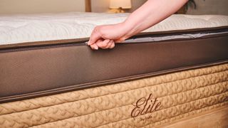 Zipping the cover of the Helix Midnight Elite Mattress, which has a white pillow top and brown and beige border