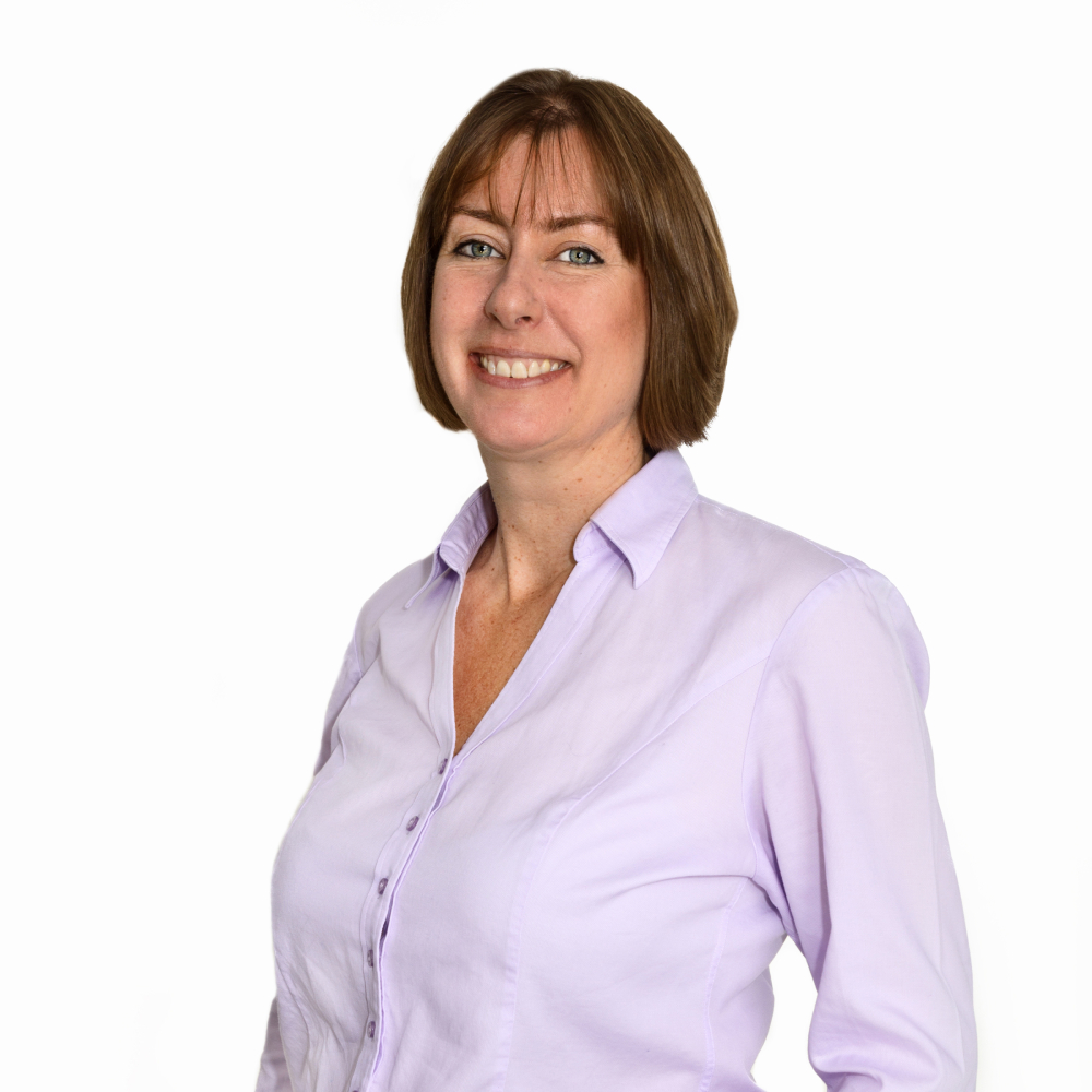 female with short brown bob wearing lilac shirt smiling at camera