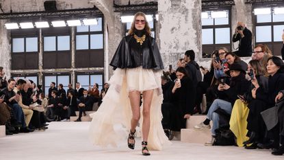 chloe aw24 runway model wearing black leather cape and white mini dress with white cape