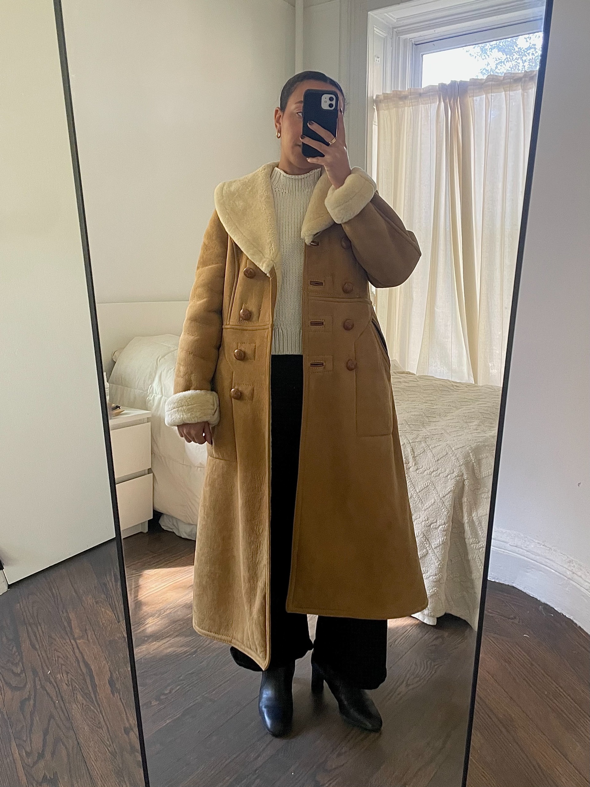 Lauren Tappan wearing a shearling coat, a beige sweater, black pants, and black boots