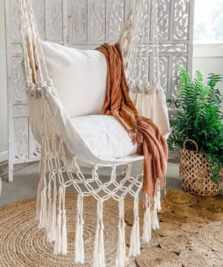 A macrame hanging chair with a jute rug underneath it and a plant next to it