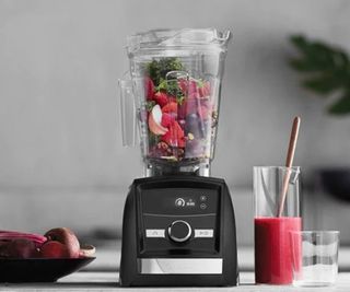 Vitamix Ascent A3300 on countertop making beetroot jucie with fruit inside, beetroots on the counter and a glass of pink drink to the right