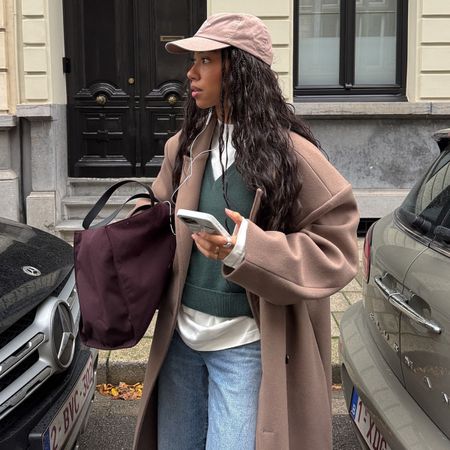Woman in camel coat, green sweater and jeans