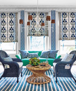 Living room with blue rattan chairs, a bright green sofa, blue and white patterned cushions and window blinds, blue and white striped rug on the floor.