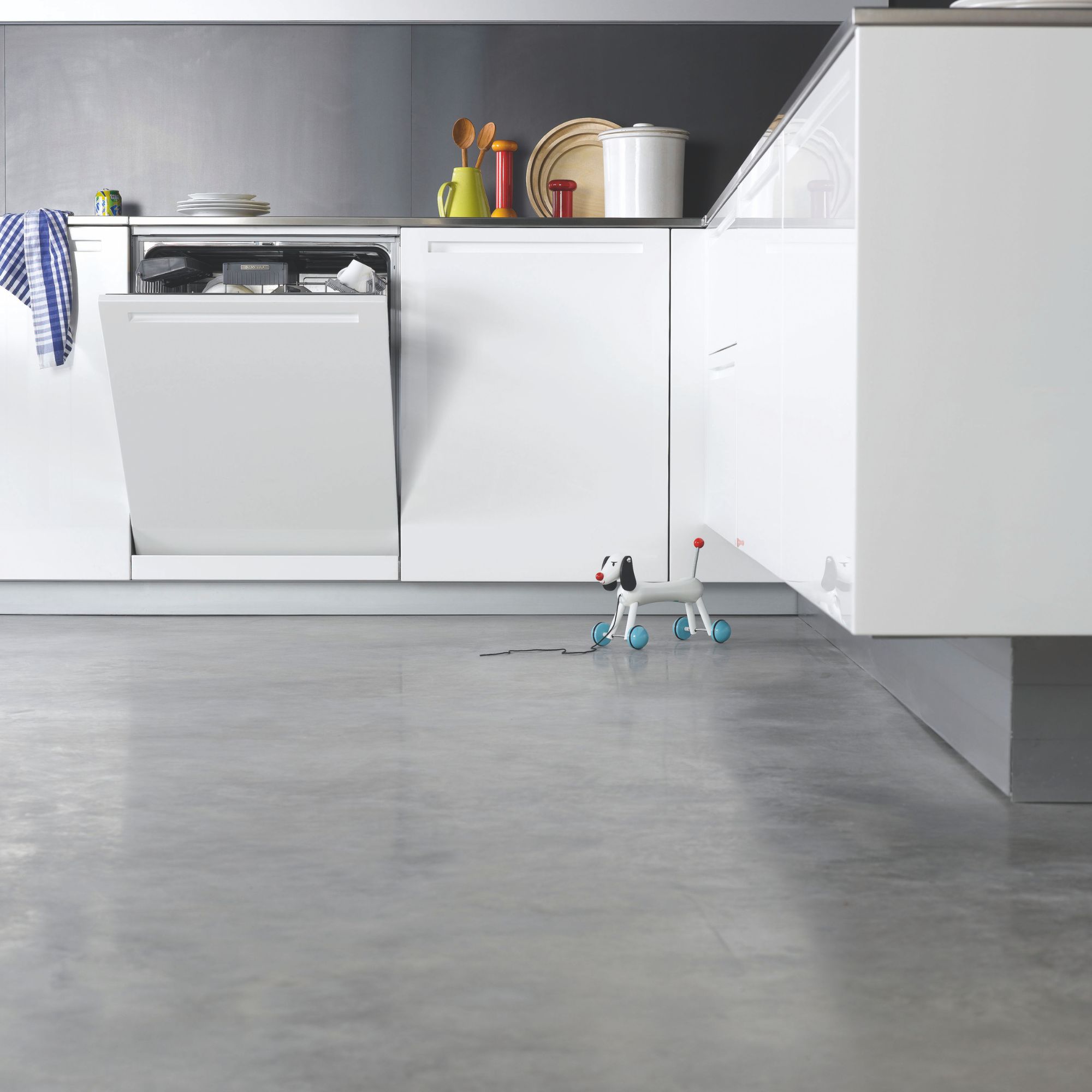 Polished concrete flooring in contemporary minimalist kitchen, with open dishwasher and child's toy on the floor