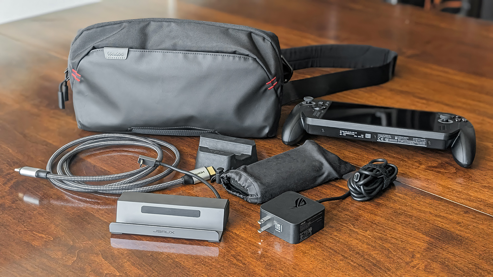 The Tomtoc Arccos G-47 Travel Bag next to an Xbox Ally X, HDMi cable, docking station, power bank, Xbox Ally X charger, and Xbox Ally X cardboard stand.