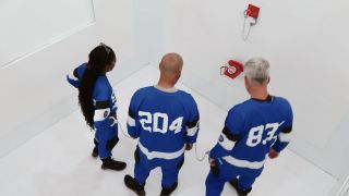 Three Beast Games contestants in a white room looking at a red phone