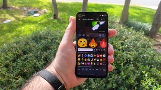 Emoji mashups on Gboard on an Android phone held up in one hand outdoors.
