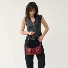 Model wearing a black zip up vest and black trousers holding a red handbag sold at Vagabond