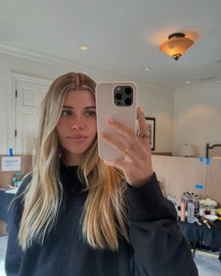 Sofia Richie Grainge wearing a black crewneck sweatshirt in a mirror selfie with her pink phone case.