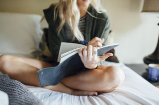 How to manifest: Low section of woman writing diary while sitting on bed