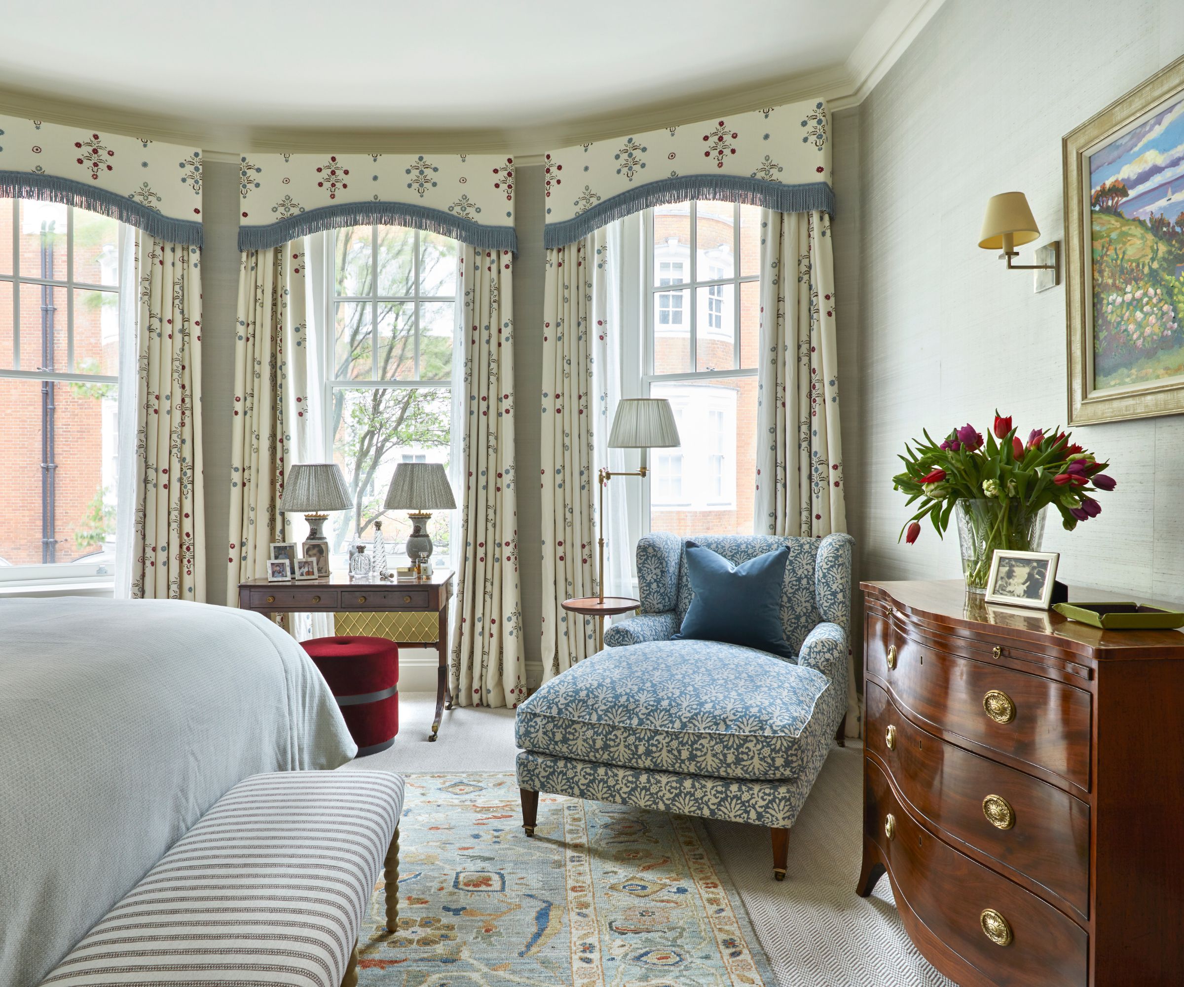 Bedroom with mahogany dresser, canopy curtains, persian rug, striped bench, blue armchair