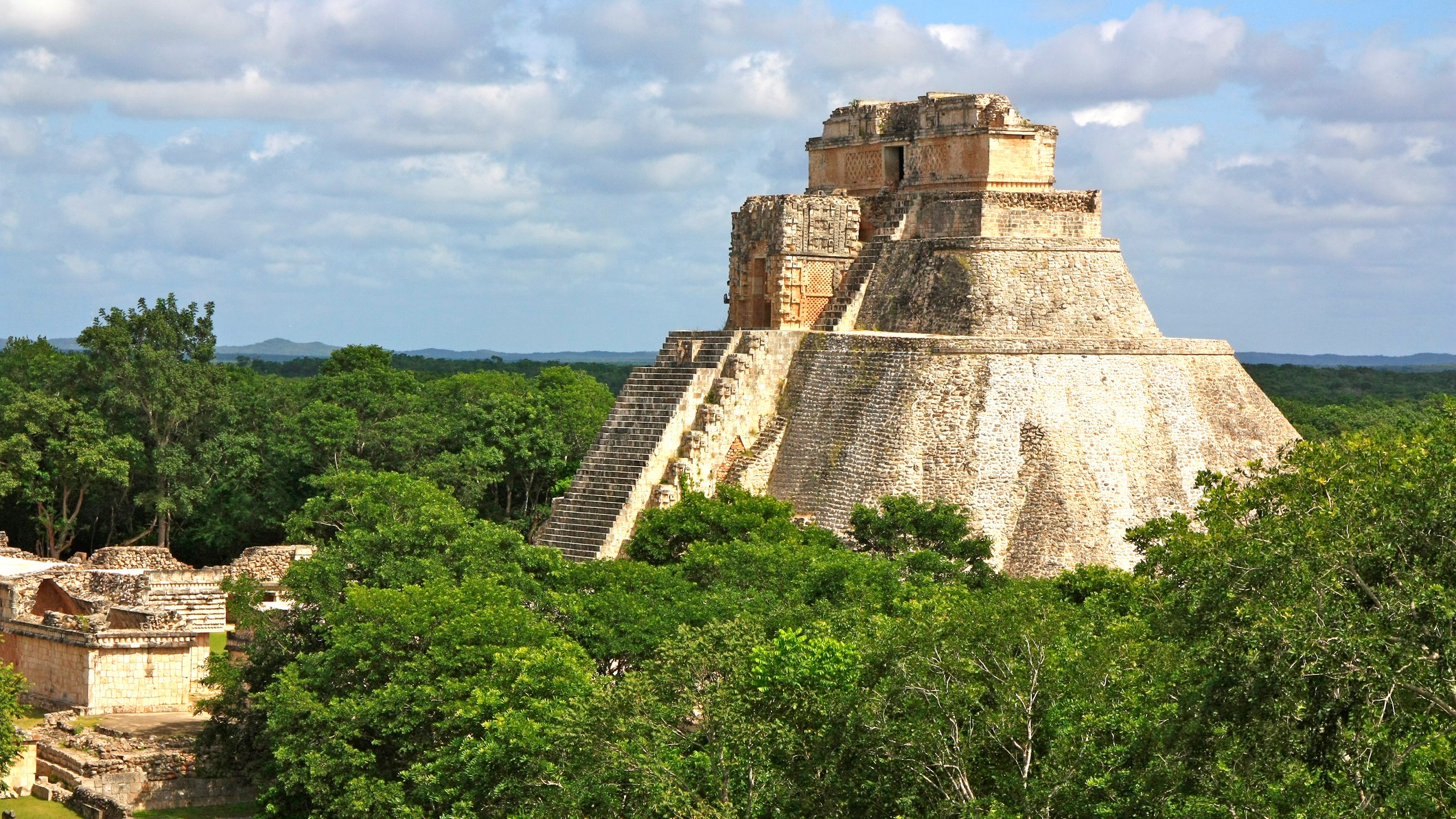 a large pyramid structure with a large staircase, rises high above the dense tree canopy below.