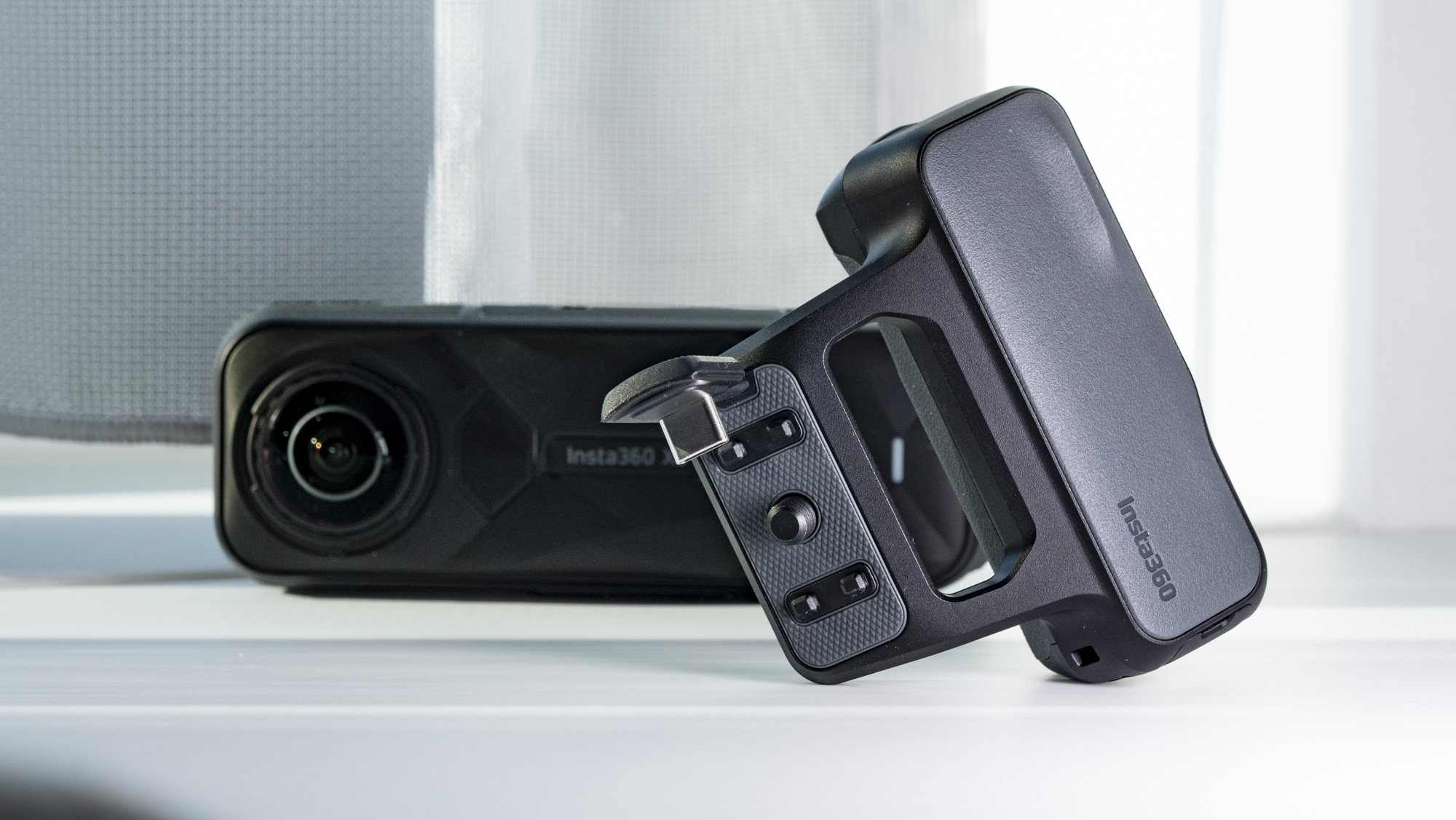 Insta360 X5 Photography Grip alongside to the camera, on a plain white surface