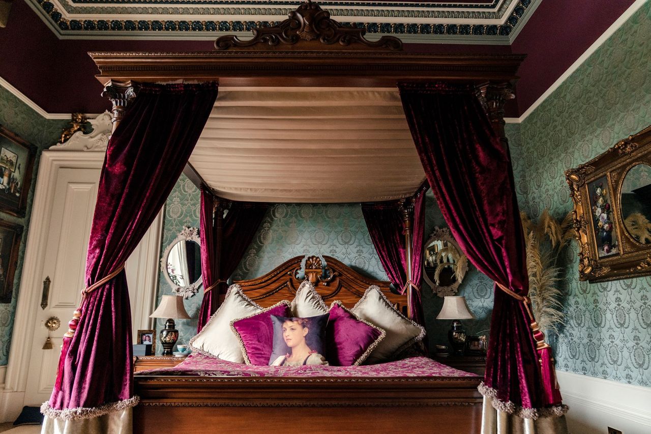 The bedroom includes a bed mocked with claret drapes and coverings with the room having green wallpaper and an en suite bathroom