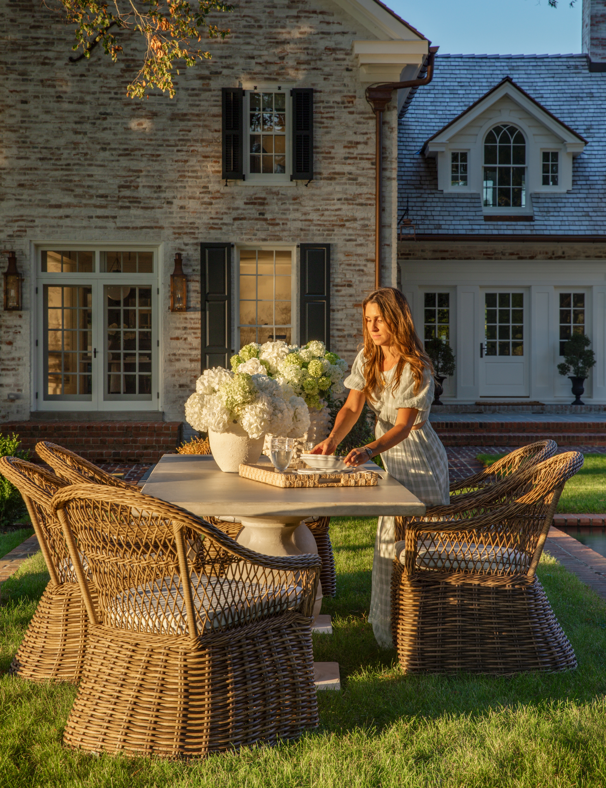 Jess Weeth setting an outdoor double pedestal dining table in the backyard of a stately New England-style brick home
