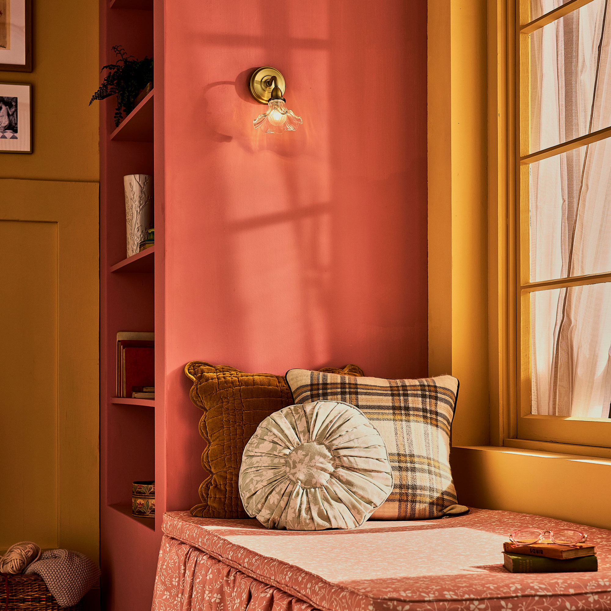 Pink painted shelves and yellow window frames with a upholstered bench and three scatter cushions
