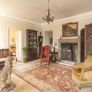 hallway with large fireplace, 2 armchairs, grandfather clock, stone dog statue and red and beige patterned rug