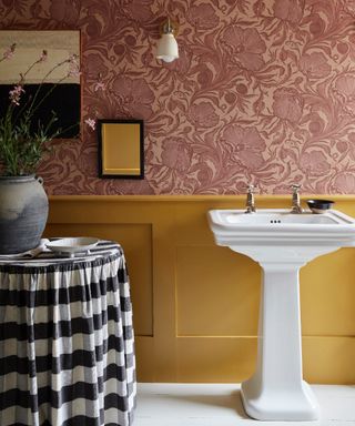 Guest bathroom with yellow paneling and coral floral wallpaper, monochromatic small tablecloth, vase of flowers, artwork, wall light