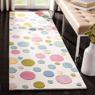 A cream runner rug with pink, blue, and orange polka dots sits on a black floor